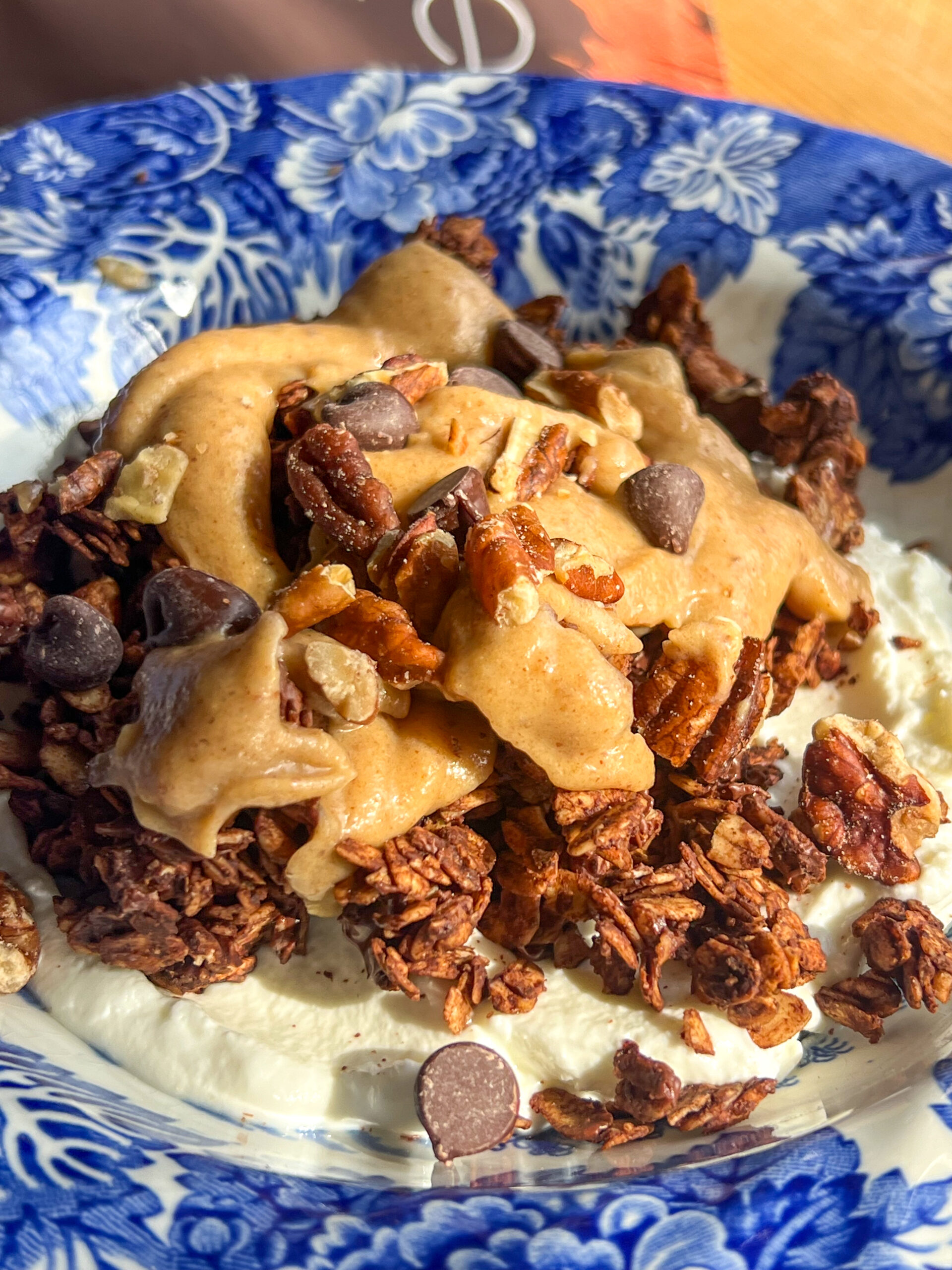 mocha turtle granola in blue bowl with peanut butter