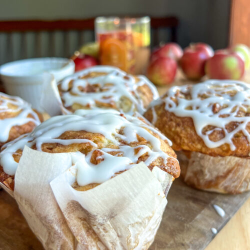 apple fritter muffins on a cutting board with apples behind it