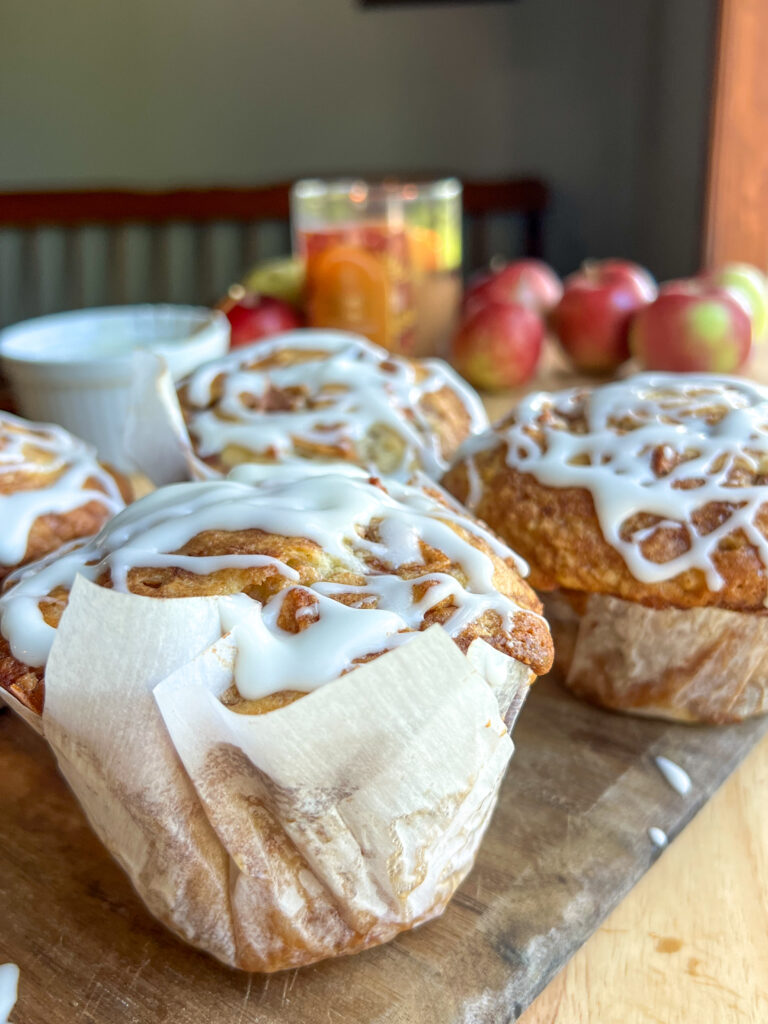 apple fritter muffins on a cutting board with apples behind it