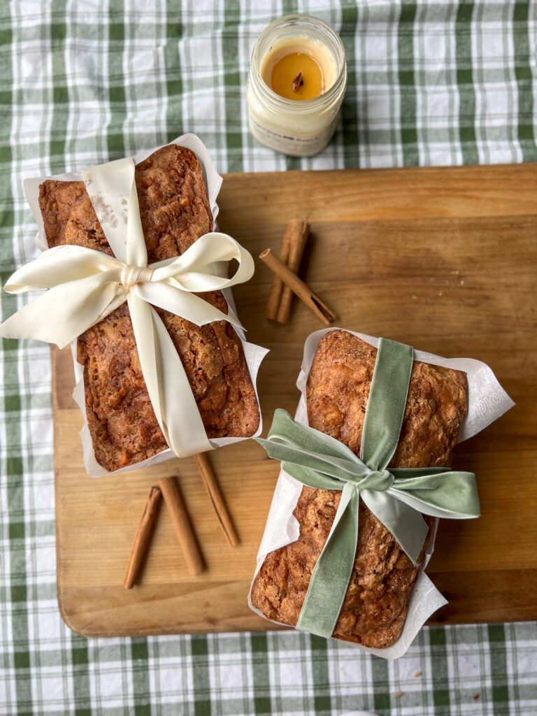 Overhead shot of apple cinnamon loaf cakes tied with ribbon on cutting board with green check tablecloth